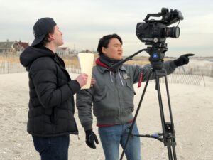 Jonathan Roberts directing a beach shoot with a Sony FX7 cinema camera while a collaborator holds the screenplay